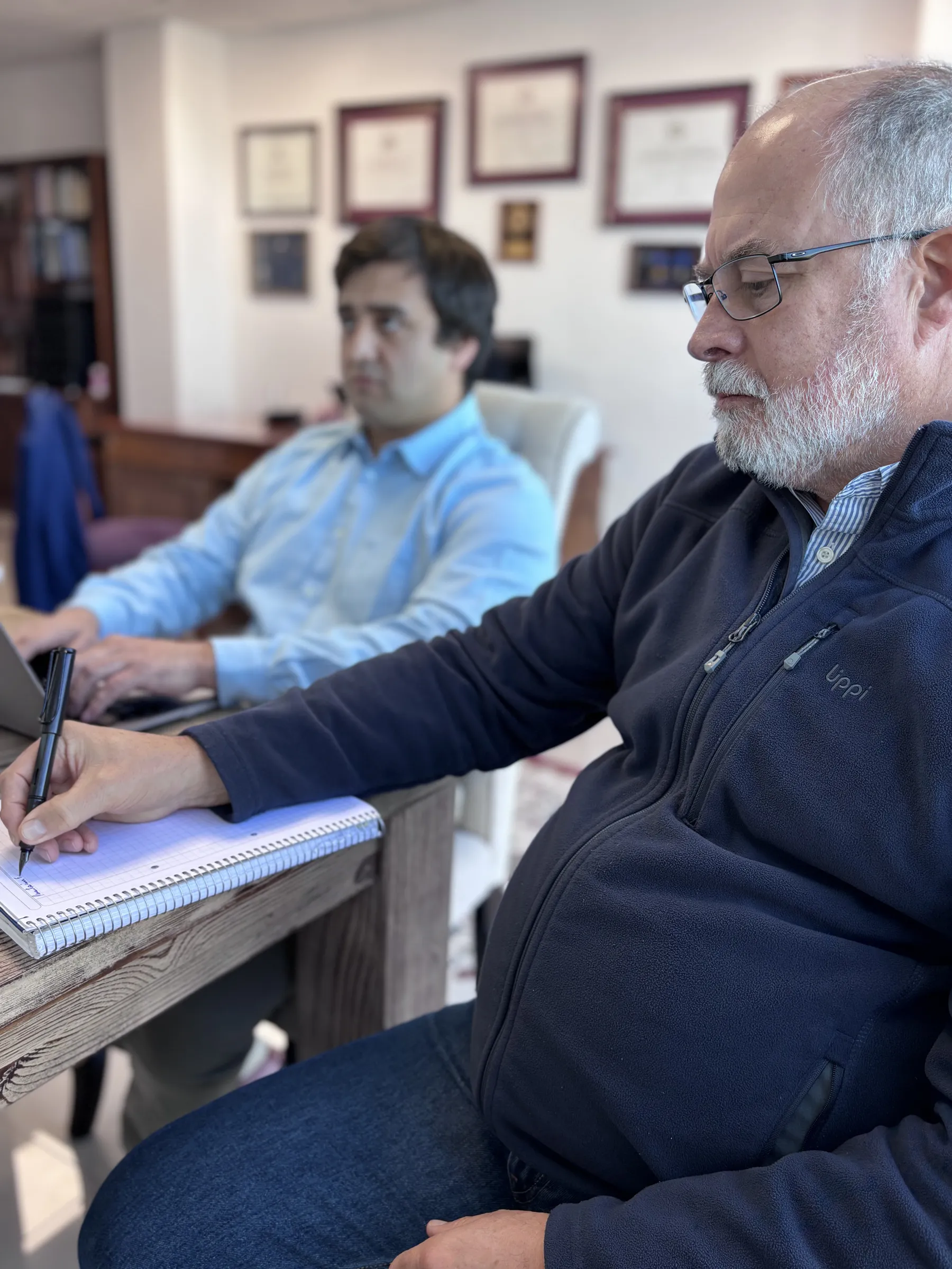 El equipo de CLM trabajando en sesión — diplomas y credenciales al fondo